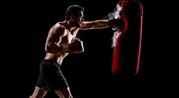 Boxer training to strengthen his chin for boxing, punching a red heavy bag with force.