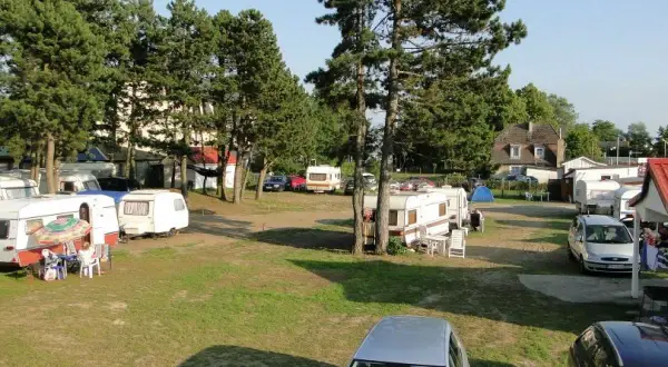 Wypoczynek na kempingu nad Bałtykiem w Mielnie. Przyczepy kempingowe i samochody na trawiastym terenie, otoczone drzewami.