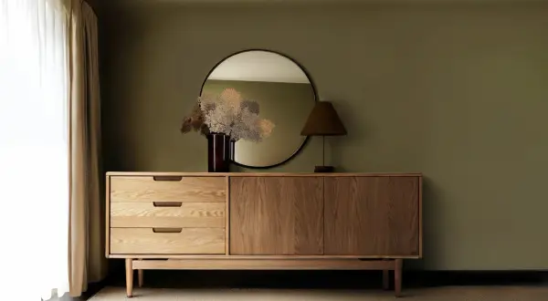 Ein Sideboard aus Holz mit Schubladen und Türen, darüber ein Spiegel und eine Lampe. So sieht ein praktisches Sideboard aus.
