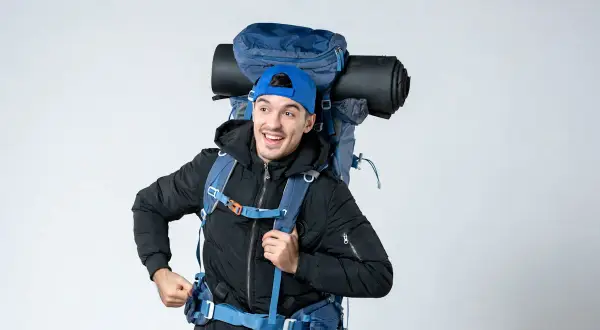 Un jeune homme souriant avec un grand sac à dos bleu, prêt pour l'aventure. On se demande : sac 70 litres combien de kilos ?