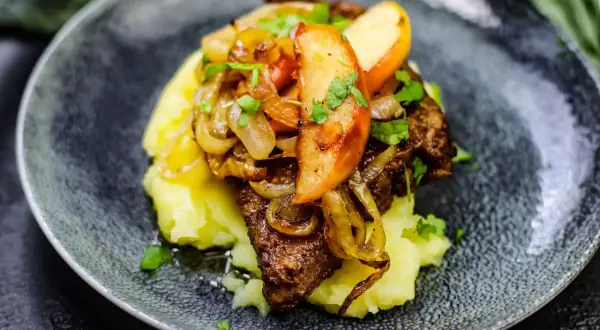 Leber Berliner Art auf Kartoffelpüree mit karamellisierten Zwiebeln und Apfelscheiben, garniert mit Petersilie.
