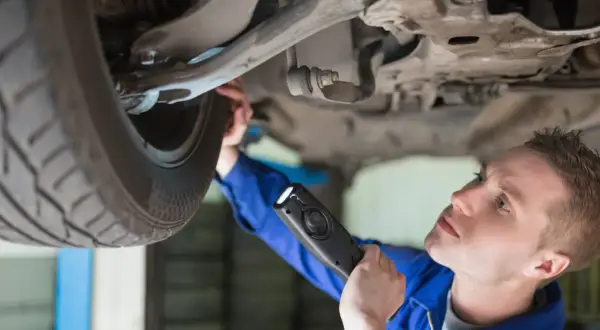 Mechanik z latarką bada podwozie auta. Czy to znak, że nastąpił brak przeglądu powyżej 30 dni?