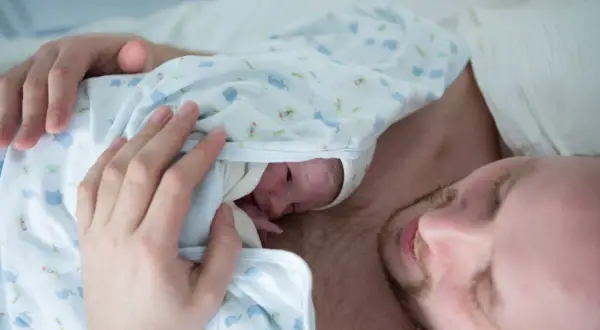 Pierwsze kangurowanie po cc. Ojciec tuli noworodka na swojej klatce piersiowej, otulając go w kocyk z motywem słoni.