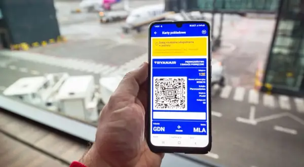 Na ekranie smartfona widać, jak wygląda bilet lotniczy Ryanair: kod QR, numer rezerwacji, miejsce 12E i trasę Gdańsk-Malta.
