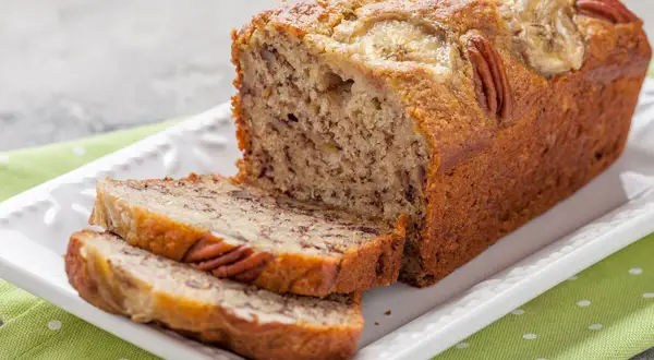 Pyszny chlebek bananowy z 2 bananów, z orzechami pekan i plasterkami banana na wierzchu, podany na białej paterze.