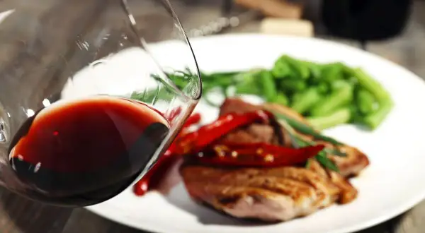 Czerwone wino w kieliszku, idealne do wieprzowiny z papryczkami chili i zieloną fasolką. Pyszny obiad czeka!