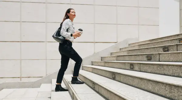 Frau steigt Treppen hoch, Kaffee in der Hand. Ein guter Weg, um abzunehmen durch gehen und fit zu bleiben.