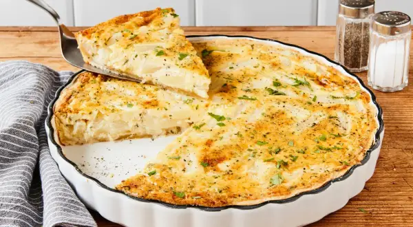 Eine köstliche Spargel Quiche wird serviert. Ein Stück wird mit einem Tortenheber herausgehoben, garniert mit frischer Petersilie.