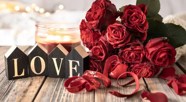 Drewniane domki z napisem LOVE, bukiet czerwonych róż i świeca tworzą romantyczną atmosferę na 11 rocznicę ślubu.