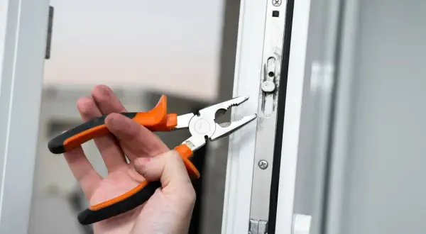 Dłoń z kombinerkami reguluje mechanizm okna, przygotowując je do trybu zimowego.