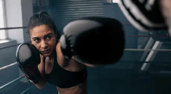 Woman in boxing gloves throws a punch during an intense boxing workout online.