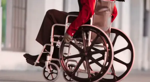 Osoba na wózku inwalidzkim w czerwonej koszuli i czarnych spodniach porusza się po chodniku.