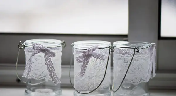 Drei hübsch gestaltete Windlichter aus Glas mit zarter Spitze und Schleifen.