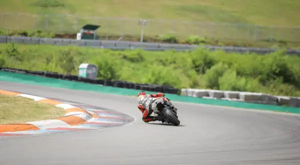 Motocyklista w czerwonym kombinezonie pochylony na zakręcie toru wyścigowego.