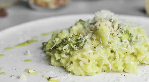 Kremowe risotto ze szparagami, posypane parmezanem i migdałami, na białym talerzu.