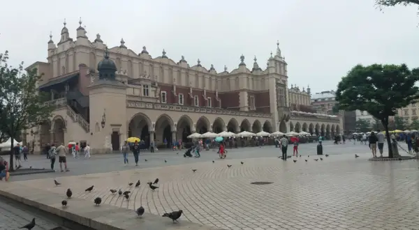 Deszczowy dzień na Rynku Głównym w Krakowie. Ludzie z parasolami spacerują, szukając schronienia w Sukiennicach lub kawiarniach. To świetny pomysł, co robić w Krakowie, gdy pada.