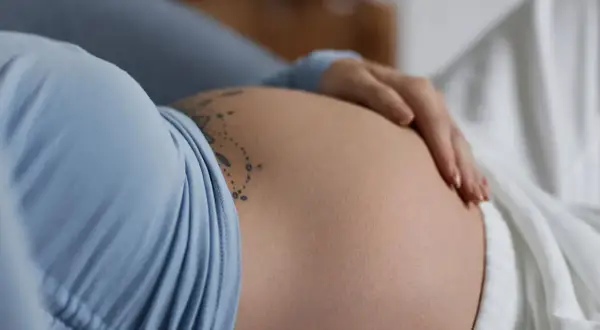 Dłoń delikatnie głaszcze ciążowy brzuch, na którym widnieje tatuaż. To piękny obraz stawiania się macicy i oczekiwania na nowe życie.