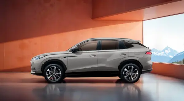 Elegancki SUV marki MG w kolorze piaskowym, zaparkowany w nowoczesnym wnętrzu z widokiem na góry.