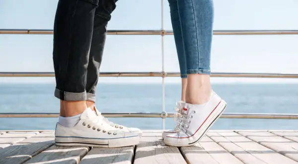 Para na drewnianym pomoście, w białych trampkach i jeansach. Idealne converse stylizacje damskie na letni dzień nad morzem.