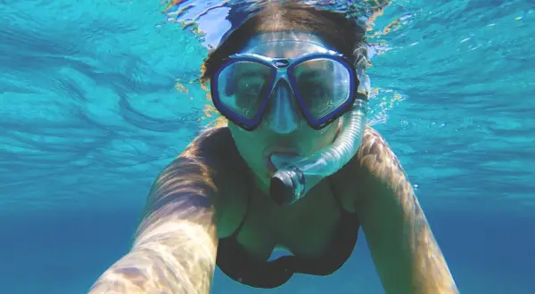 Kobieta w masce do snorkelingu, pokazująca, jak działa maska do snorkelingu, oddychając pod wodą.