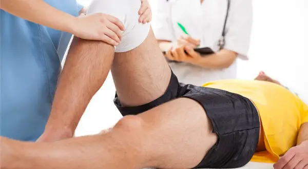 Fizjoterapeuta pomaga pacjentowi w ćwiczeniach po rekonstrukcji ACL. Rehabilitacja kolana jest kluczowa.