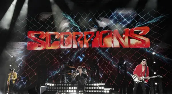 Zespół Scorpions na scenie z dużym logo zespołu i efektami świetlnymi.