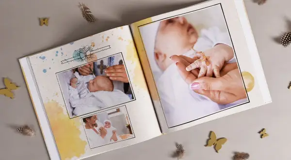 Otwarta księga pamiątkowa z fotografiami niemowlęcia, ozdobiona piórkami i motylkami.