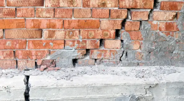 Uszkodzona ceglana ściana i pęknięty betonowy stopień świadczą o problemach z podbijaniem fundamentów.