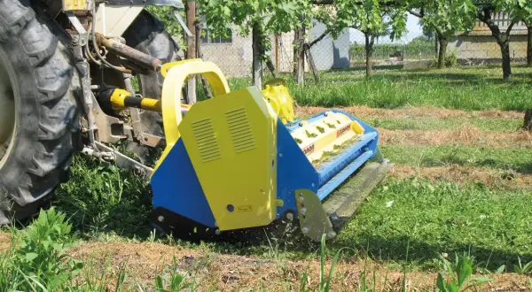 Trattore con falciatrice gialla e blu che lavora in un vigneto. L'erba tagliata copre il terreno, un segno di potenziale inquinamento del suolo se non gestita correttamente.