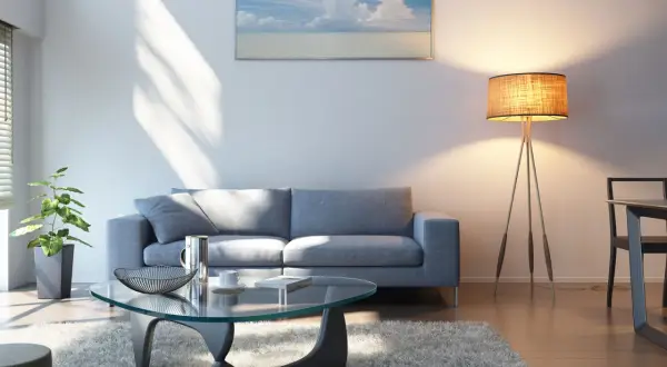 Ein helles Wohnzimmer mit grauem Sofa, Glascouchtisch und einem Bild mit Meerblick. Welche Farbe passt zu grauem Sofa? Hier sehen wir helle Töne, die gut harmonieren.