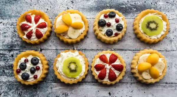 Kolorowe tartaletki z owocami: truskawki, kiwi, borówki, maliny i morele na kremowym nadzieniu.