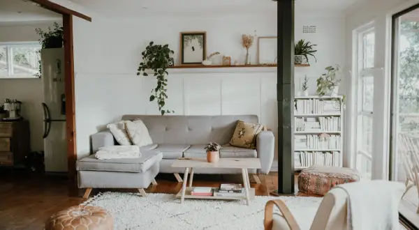 Ett ljust vardagsrum med grå soffa, träbord och bokhylla. Gröna växter och konst ger en känsla av skandinavisk minimalism.