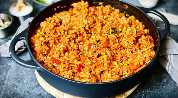Herzhafter Djuvec Reis mit Mais und Paprika in einer Gusseisenpfanne, bereit zum Servieren.