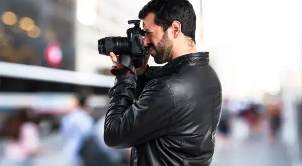 Un fotoreporter con giacca di pelle cattura un momento in strada, mostrando il vero significato del suo mestiere: documentare la realtà.