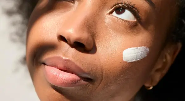 Geste doux pour mettre de la crème sur la joue d'une jeune femme, illuminée par la lumière du soleil.