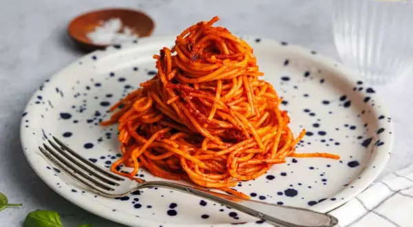 Ein Berg aus gekochte spaghetti braten mit Tomatensauce auf einem Teller mit blauen Tupfen. Eine Gabel liegt daneben.