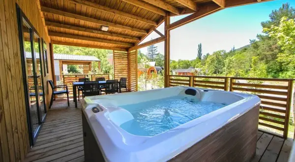 Terrasse en bois avec jacuzzi et table à manger, vue sur la nature. Idéal pour un séjour détente au camping de la ferme.