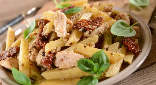 Penne z kurczakiem i suszonymi pomidorami, udekorowane świeżą bazylią. Pyszne danie na obiad.