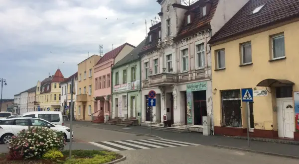 Kolorowe kamienice w **Złotnikach Kujawskich** przy ulicy, z samochodami i zielenią.