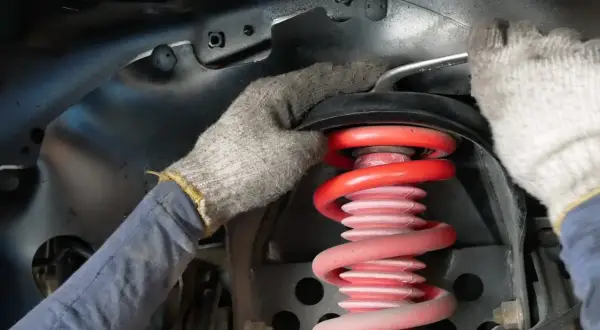 Mechanik w rękawiczkach dokonuje wymiany sprężyny amortyzatora w samochodzie.