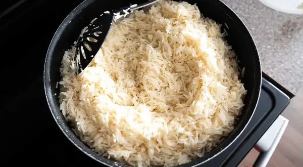 En stor kastrull med fluffigt, vitt ris står på spisen. En svart slev rör om i det nykokta riset, redo att serveras. Perfekt för en snabb middag, detta ris i kylen är en räddare i nöden.