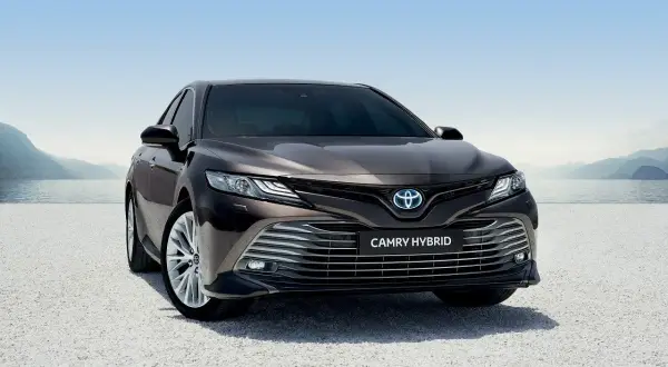 Elegancka, ciemnobrązowa Toyota Camry Hybrid 2020 zaparkowana nad jeziorem, gotowa na podróż.