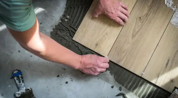 Man placing wood-look tiles on cement floor. Learn como colocar el parquet horizontal o vertical para un acabado perfecto.