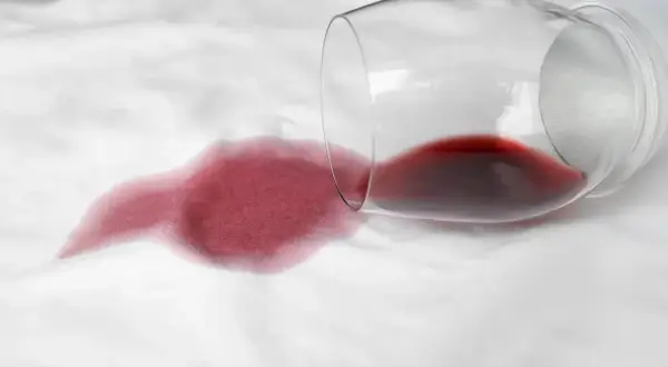 Un bicchiere di vino rosso rovesciato su un tessuto bianco crea macchie che non vanno via con la candeggina.