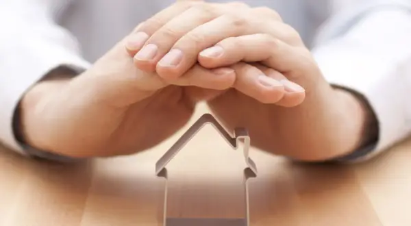Mani che proteggono una casetta, simbolo di un comproprietario non vuole vendere.