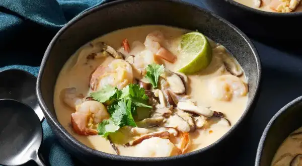 En skål med krämig tom ka gai med räkor, svamp och koriander. En limeklyfta flyter på ytan.