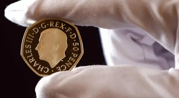 Złoty suweren moneta z wizerunkiem Karola III, trzymana w białej rękawiczce.