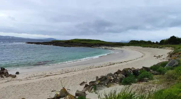 La serena playa Santa Marta de Cangas, con sus aguas turquesas y arena dorada, invita a la calma bajo un cielo nublado.