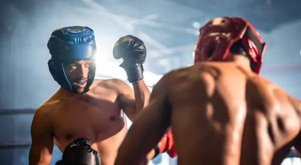 Two boxers in a ring, wearing headgear and gloves, engage in sparring. The intense training session highlights their focus and determination.