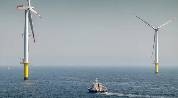 Ogromne turbiny wiatrowe na morzu, symbol nowoczesnej morskiej energetyki wiatrowej, na tle spokojnego oceanu. Statek serwisowy płynie w kierunku jednej z nich.